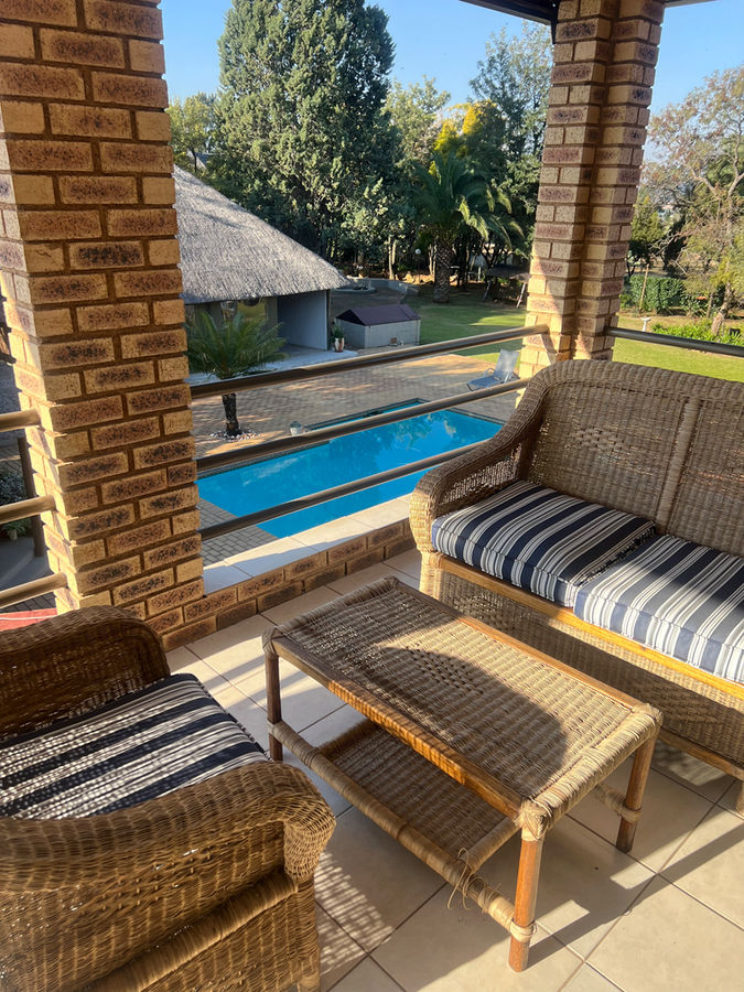 A shaded lodge patio overlooking the swimming pool and thatched accommodation at Protea Ridge.