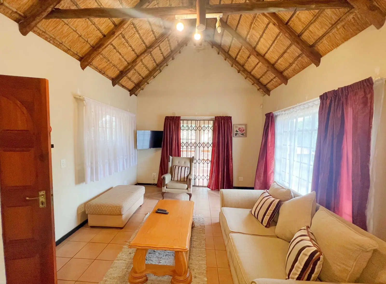 A lounge beneath a high thatched ceiling with seating and a television.