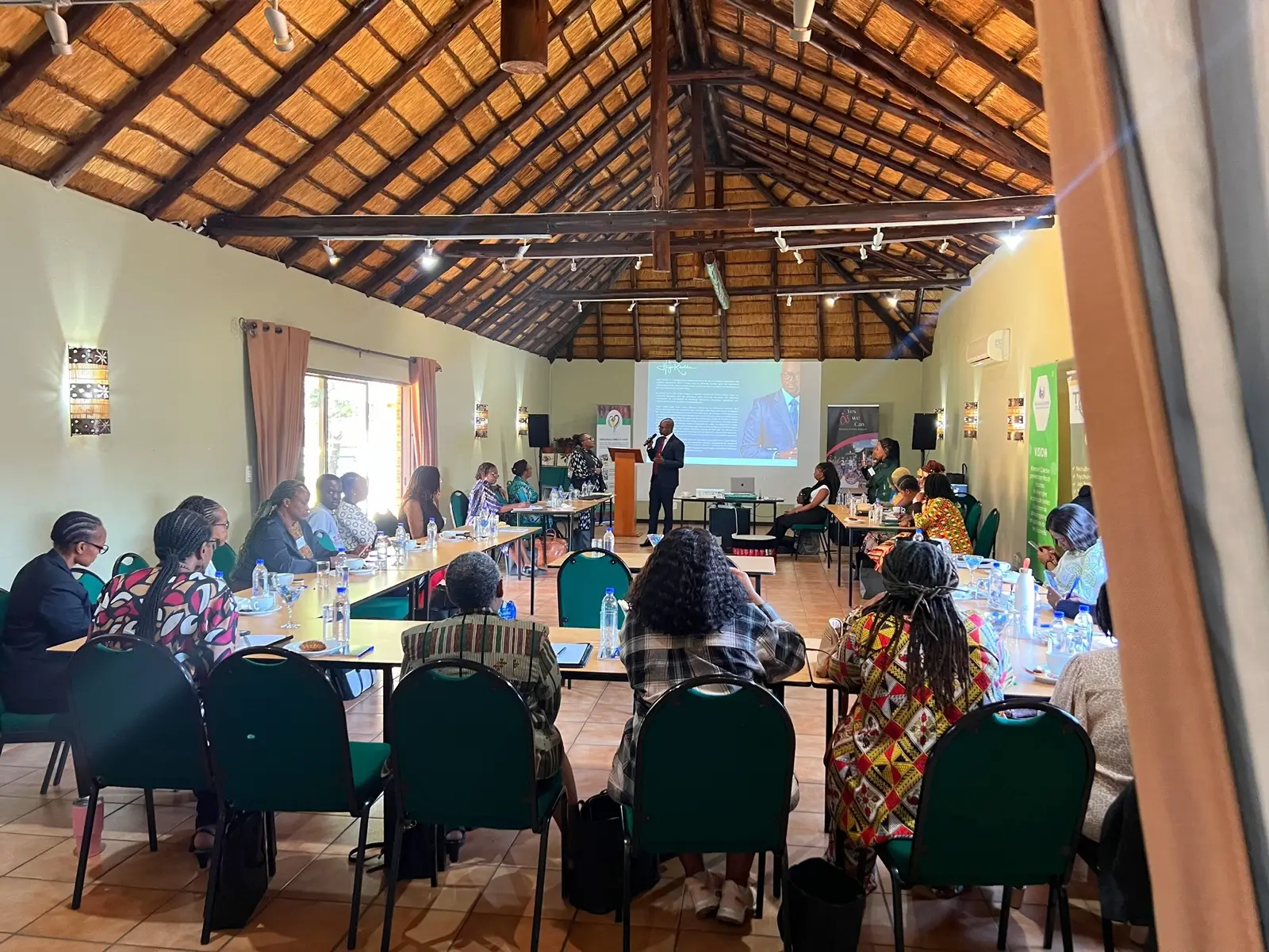 A conference session in the thatched event hall with a projection screen.