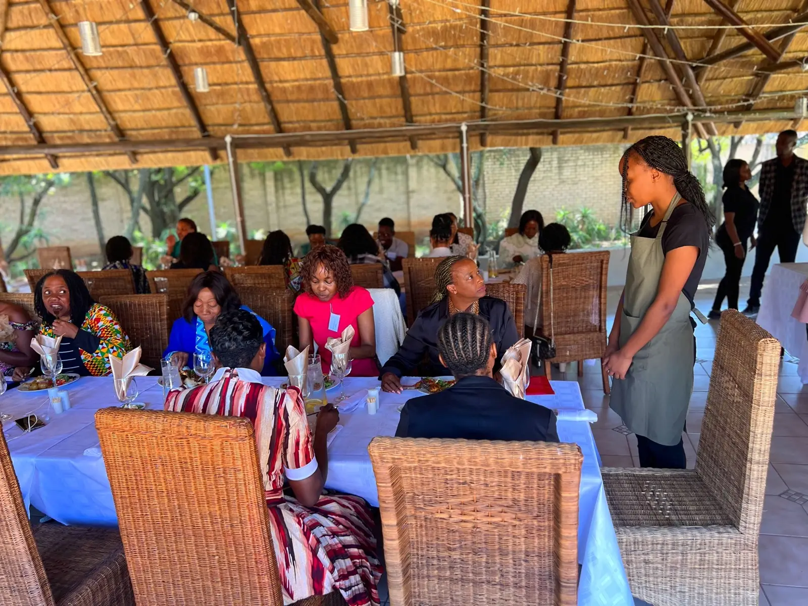 Waiters serving guests at tables in the thatched dining hall.