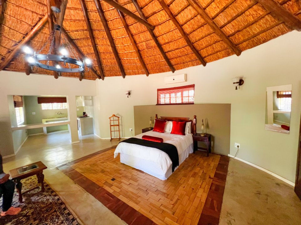 A thatched suite with a double bed, timber ceiling and open bathroom area.