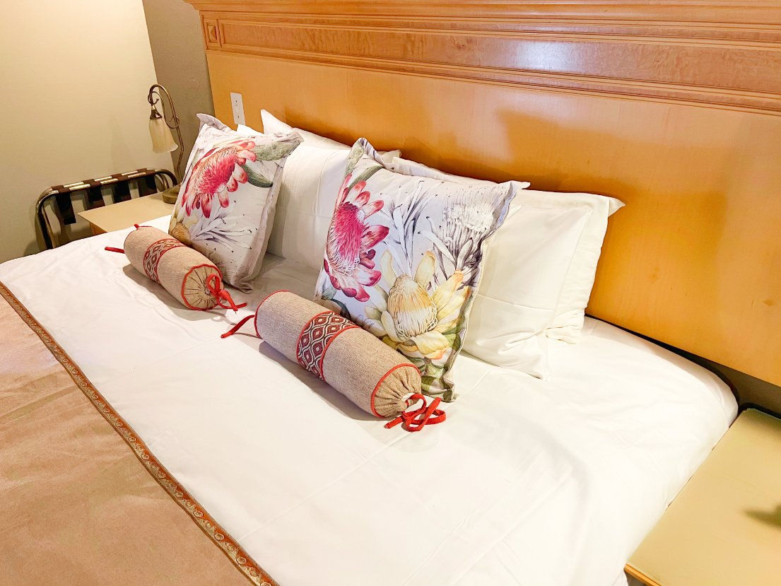 A neatly made bed with floral cushions and warm timber detailing.