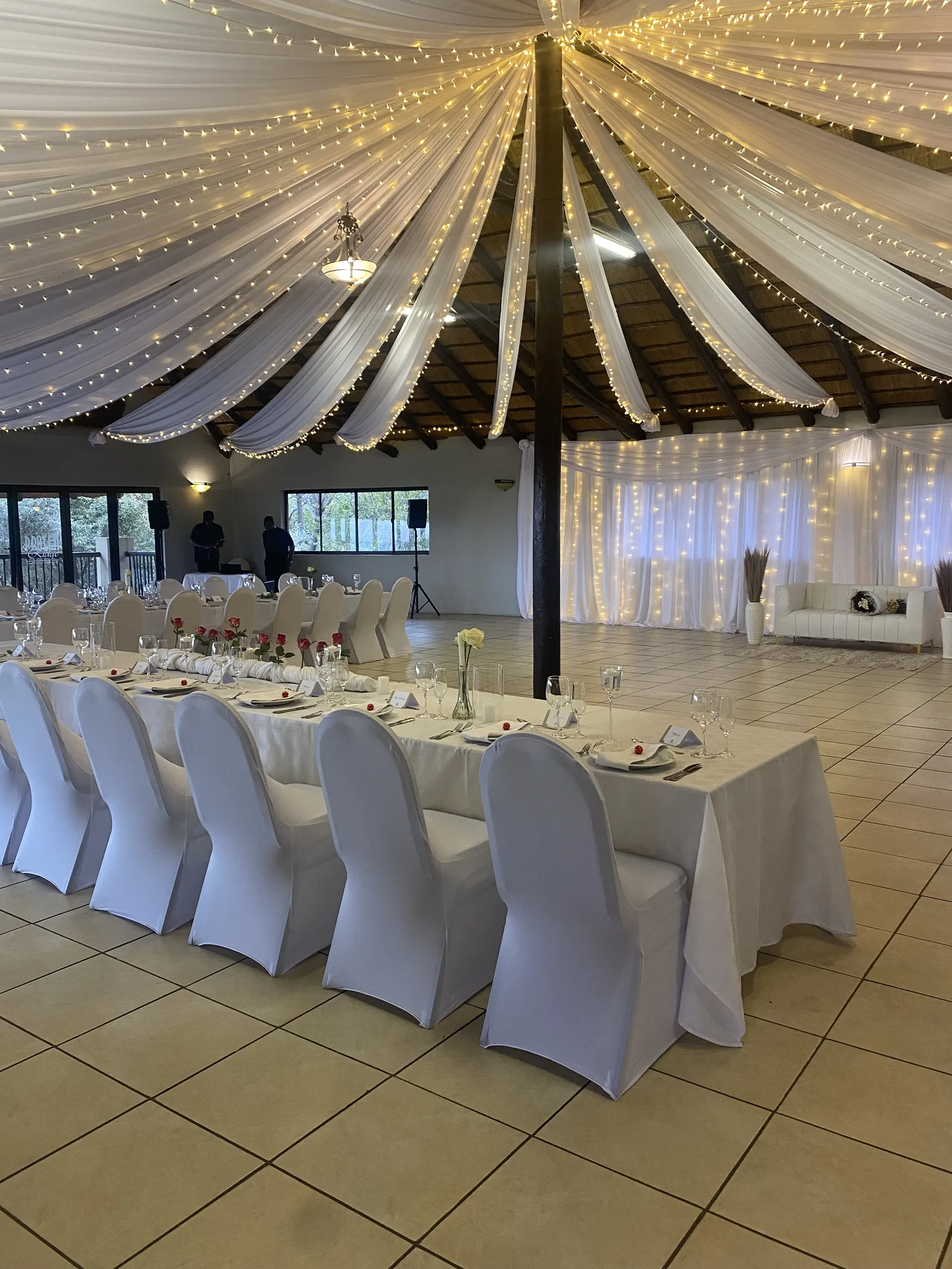 A wedding reception room with white chair covers and draped ceilings.